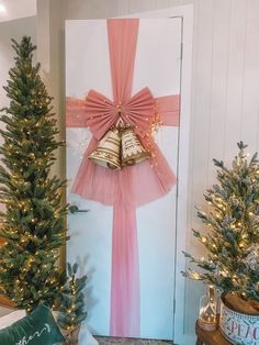 christmas trees and bells in front of a door decorated with pink tulle, bows and gold bells