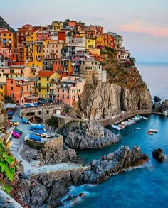 an aerial view of colorful buildings on the cliff by the ocean with boats in the water