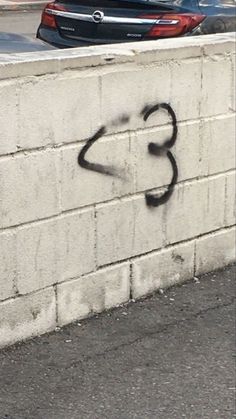 graffiti is spray painted on the side of a wall next to a parking lot with parked cars