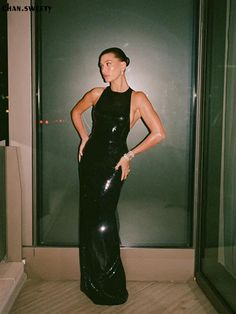 a woman in a black dress standing next to a glass wall with her hands on her hips