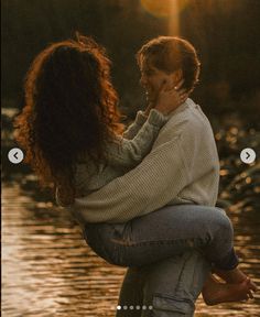 two people standing next to each other in front of the water with their arms around each other