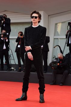 a man standing on top of a red carpet next to a group of people wearing sunglasses