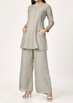 A two-piece palazzo set, seamlessly blending Indo-Western fusion for a comfortable and sophisticated appearance. This ensemble, in a refined pearl grey hue, comprises a short-length kurta paired with palazzo pants. The plain top, featuring full-length sleeves subtly highlighted with sequins, emanates an understated elegance. The kurta is additionally adorned with pockets on both sides, while the inclusion of plain palazzo pants completes this stylish and poised look.  Note: Colors may slightly v Wide Leg Palazzo Set For Wedding, Designer Wide Leg Sets For Eid, Designer Wide Leg Palazzo Set For Eid, Elegant Festive Wide Leg Palazzo Set, Festive Wide Leg Sets For Eid, Elegant Festive Pant Set With Wide Legs, Elegant Festive Wide Leg Pant Set, Elegant Wide-leg Pant Set For Festive Occasions, Elegant Wide Leg Pant Set For Festive Occasions