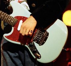 a close up of a person holding a red and blue guitar in their hand while standing on stage