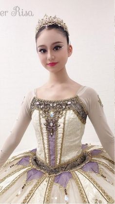 a young ballerina in a white and purple dress posing for the camera with her hands on her hips