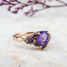 The Royal Amethyst ring exudes timeless luxury with its pear-cut natural amethyst centerpiece, a gemstone long associated with nobility and spiritual power. The vintage-inspired design is enhanced by three round-cut amethysts on each side, delicately framing the central stone, giving it a regal aura. The rose gold setting complements the deep purple hues of the gemstones, creating an opulent contrast that feels both luxurious and elegant. This ring offers a touch of royal elegance, perfect for someone seeking a statement piece with a timeless appeal. 𝗗𝗘𝗧𝗔𝗜𝗟𝗦𝗠𝗔𝗜𝗡 𝗦𝗧𝗢𝗡𝗘𝗚𝗲𝗺𝘀𝘁𝗼𝗻𝗲: Natural Amethyst𝗖𝗼𝗹𝗼𝗿: Purple𝗦𝗵𝗮𝗽𝗲: Pear 6*9.0mm𝗖𝘂𝘁: Full𝗠𝗲𝗮𝘀𝘂𝗿𝗲𝗺𝗲𝗻𝘁: 1.5 ct approx𝗤𝘂𝗮𝗹𝗶𝘁𝘆: VS clarity gradeAmethyst are natural and can therefore slightly vary Rutilated Quartz Ring, Art Ring, Moss Agate Ring, Alexandrite Ring, Timeless Luxury, Engagement Rings Bridal Sets, Spiritual Power, Gothic Rings, Morganite Ring