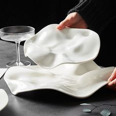 a person holding a white plate on top of a table next to a wine glass