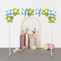 an arch made out of balloons and other items on a table with a white wall in the background