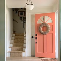 an orange door with a wreath on it in front of some stairs and a light fixture