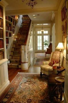 a living room filled with lots of furniture and bookshelves next to a stair case