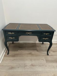 an antique desk with two drawers and gold trimmings on the top, against a white wall