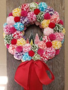 a colorful wreath hanging on the side of a wooden door decorated with pom - poms