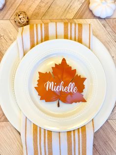 a white plate topped with an orange leaf next to a yellow and white striped napkin