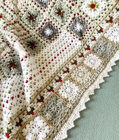 a white crocheted blanket with red and green flowers on the edges, sitting on a blue surface