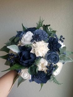 a bridal bouquet with blue and white flowers is held by someone's hand