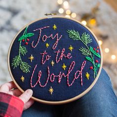 someone holding up a hand embroidered christmas ornament with the words joy to the world on it