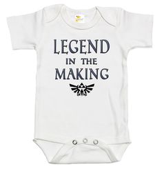 Rapunzie's adorable baby onesie, perfect for little ones who are destined to become legends! Made from 100% cotton, this short-sleeve onesie ensures utmost comfort for your precious bundle of joy. With its charming design featuring the iconic Legend of Zelda video game symbol and the captivating caption, "Legend in the Making," your baby will surely make a statement wherever they go.Crafted with love and attention to detail, this baby onesie combines style and softness to create a delightful out Pre-shrunk Short Sleeve Onesie For Playtime, Funny Short Sleeve Onesie For Birthdays, Funny Short Sleeve Onesie For Birthday, White Short Sleeve Onesie With Character Print, Funny Customizable Short Sleeve Onesie, Short Sleeve Onesie For Father's Day Gift, Cotton Short Sleeve Bodysuit With Character Print, Funny Short Sleeve Onesie, Cotton Bodysuit With Character Print And Short Sleeves