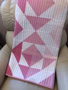 a pink and white quilt sitting on top of a couch next to a pillow in the shape of an x