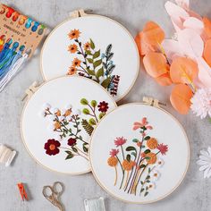 three embroidery hoops with flowers on them next to some scissors and other crafting supplies