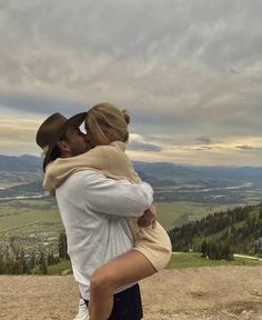 a man and woman embracing each other on top of a mountain