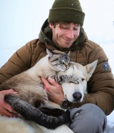 a man is holding two cats and a dog in the snow while they are cuddling