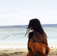 a woman sitting on top of a sandy beach next to the ocean