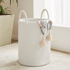 a large white basket with tassels on the handles in front of a window