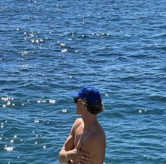 a man standing on the edge of a body of water wearing a blue hat and swimming trunks