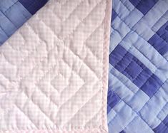 a blue and pink quilted bed spread on top of a white tablecloth with an empty piece of cloth next to it