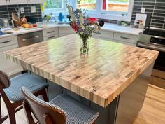 a kitchen island made out of wood with chairs around it and flowers in a vase on top