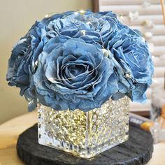 a blue flower in a square vase on a wooden table next to a mirror box