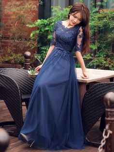 a woman in a long blue dress standing on a patio table next to a chair