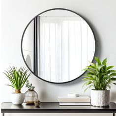 a round mirror sitting on top of a wooden table next to potted plants and books