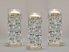 two clear glass vases with silver balls and lights on the bottom one has a lit candle in it