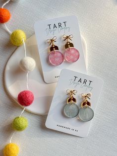 two pairs of earrings with bows and pom - poms hanging from them on a plate