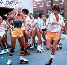 two women rollerblading down the street in front of a group of young people