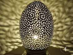 an intricately designed egg sitting on a table next to a light shadow that is cast onto the wall behind it