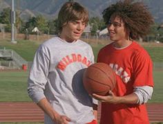 two young men standing next to each other holding a basketball