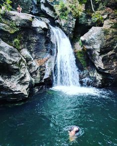 a man swimming in the water next to a waterfall