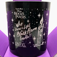 a black candle with white writing on it and stars around the edges, in front of a purple background