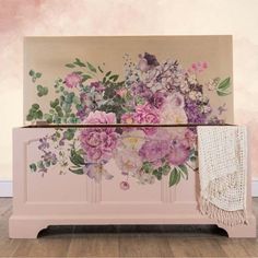 a pink chest with flowers painted on the front and sides, sitting against a wall