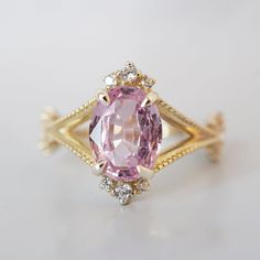 a fancy ring with an oval cut pink sapphire surrounded by small white diamonds and gold plating