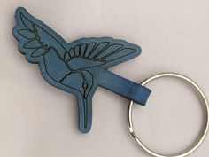 a blue bird shaped keychain sitting on top of a white table next to a metal ring