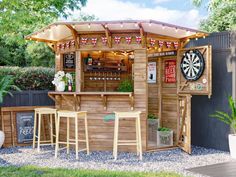 an outdoor bar with darts on the wall and wooden stools in front of it