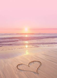 a heart drawn in the sand on a beach at sunset with waves coming towards it