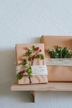 two wrapped presents sitting on top of a wooden shelf next to each other with greenery and twine