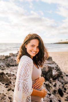 a pregnant woman standing on the beach with her belly wrapped around her waist and smiling at the camera