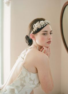 a woman in a white dress is looking at herself in the mirror with her hand on her chin