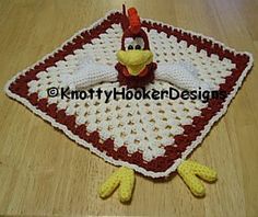 a crocheted chicken sitting on top of a wooden table next to a red and white blanket