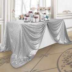 a table covered in silver cloth with presents on it next to a wall and window